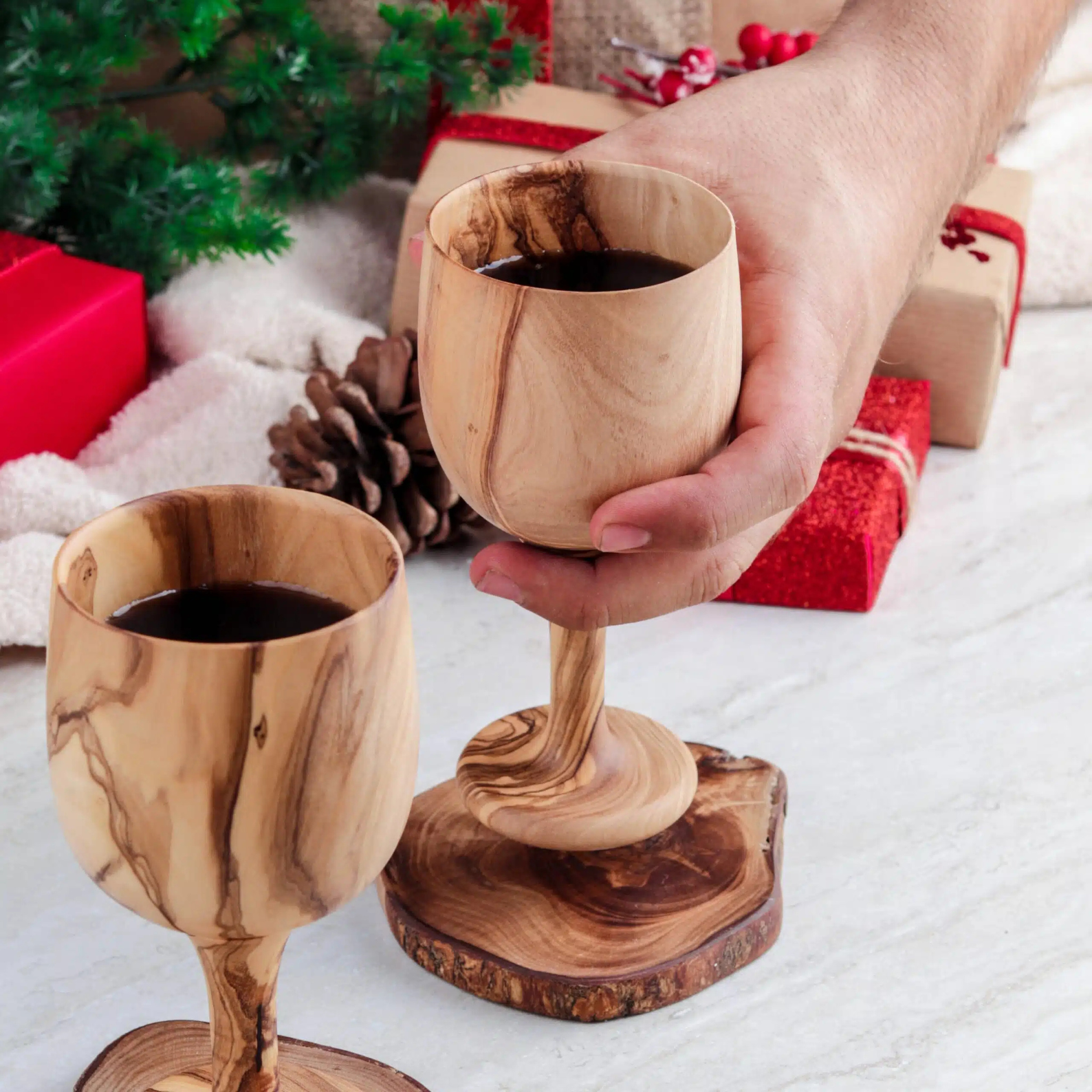 Zwei handgemachte Holzkelche aus Olivenholz neben passendem Flaschenhalter auf mediterranem Hintergrund