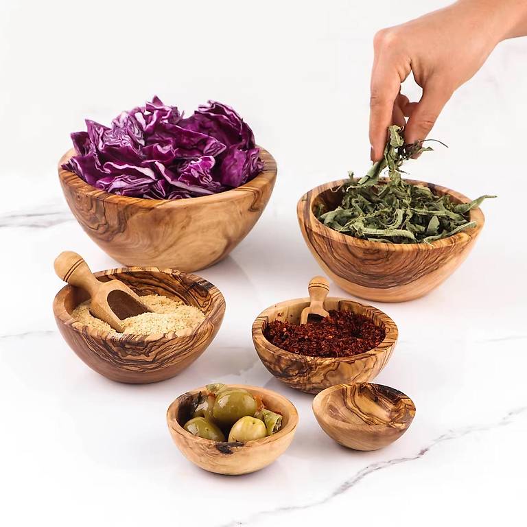 Sechs Olivenholzschalen gefüllt mit Gewürzen, Kräutern, Oliven und Rotkohl