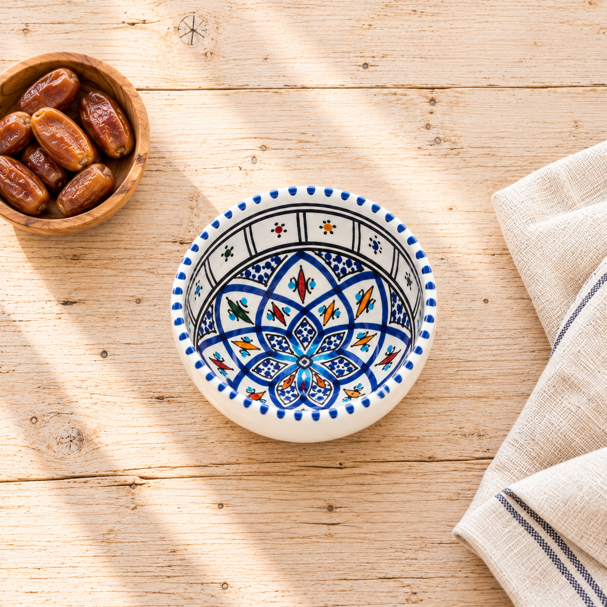 Kleine handbemalte Snackschale aus tunesischer Keramik mit Pistazien, neben einem Teeglas auf rustikalem Holztisch.